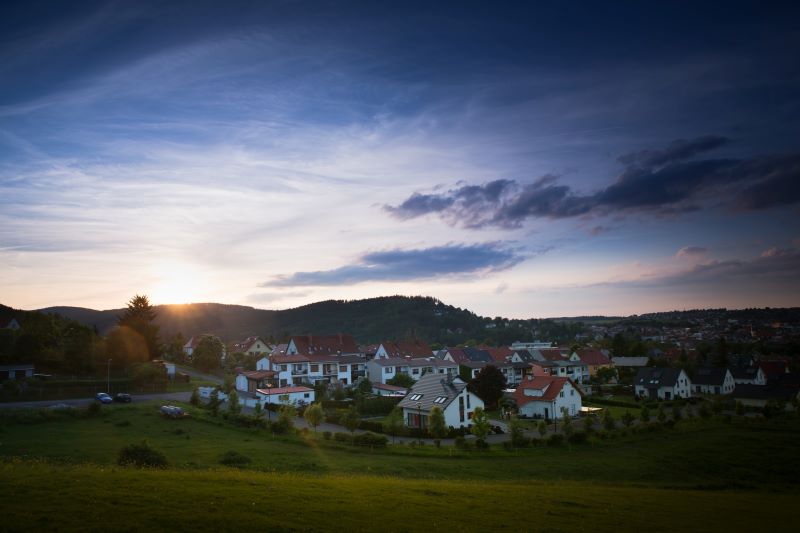 Blick auf ein Dorf am Rand eines Gebirgszuges, hinter dem gerade die Sonne aufgeht.
