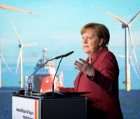 Bundeskanzlerin Merkel bei einer Rede im Hintergrund Fotos von Windkraftanlagen.