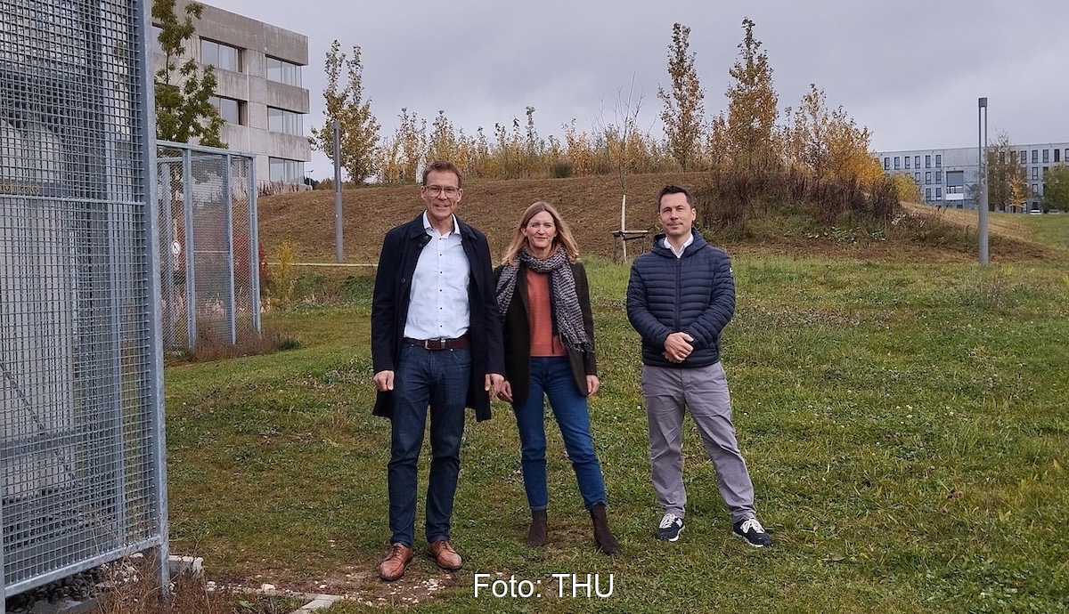 Das dreiköpfige Projektteam steht bei grauem Himmel auf der grünen Wiese im Energiepark der THU.