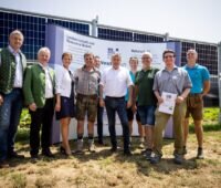 Frauen und Männer bei der Einweihung vor vertikal aufgebauten Solarmodulen.