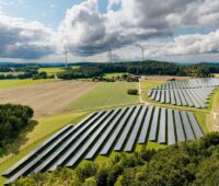 PV-Freifläche mit drei Windenergieanlagen im Hintergrund.