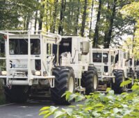 Weiß lackierte Kraftwagen mit großen Reifen in einer Reihe auf einem Waldweg. Vibro-Trucks erkunden den Untergrund, um das Potenzial für Tiefengeothermie-Bohrungen zu erkunden. Das Geothermie-Beschleunigungsgesetz macht das künftig einfacher.