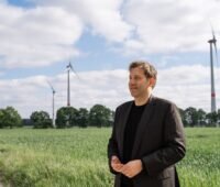 Bundesfinanzminister Lars Klingbeil im Vordergrund. Im Hintergrund Windkraftanlagen.