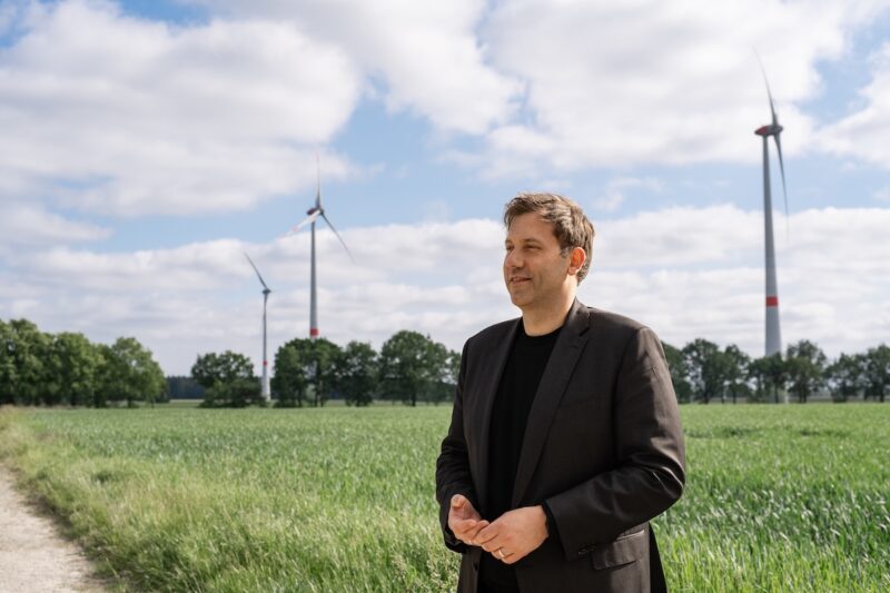 Bundesfinanzminister Lars Klingbeil im Vordergrund. Im Hintergrund Windkraftanlagen.
