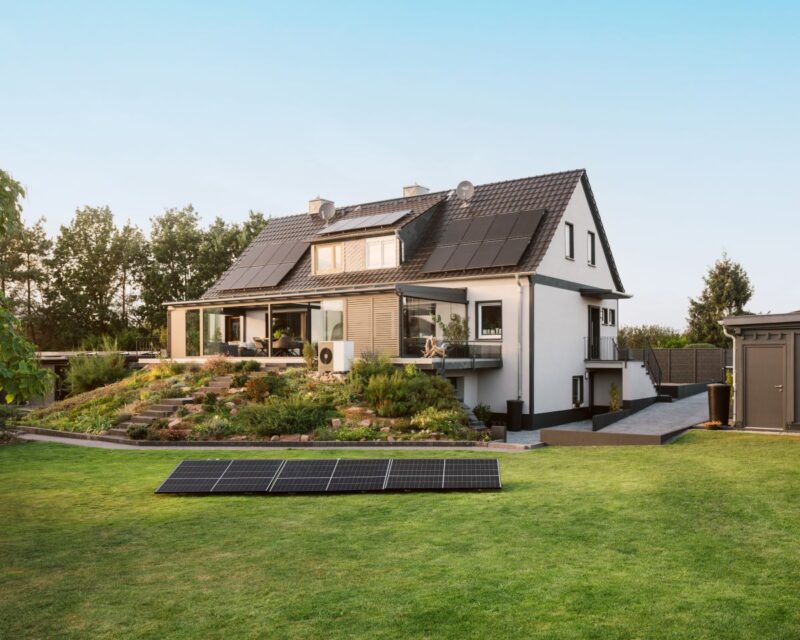 Auf dem Rasen vor einem Einfamilienhaus liegt eine Gruppe von Solarmodulen.