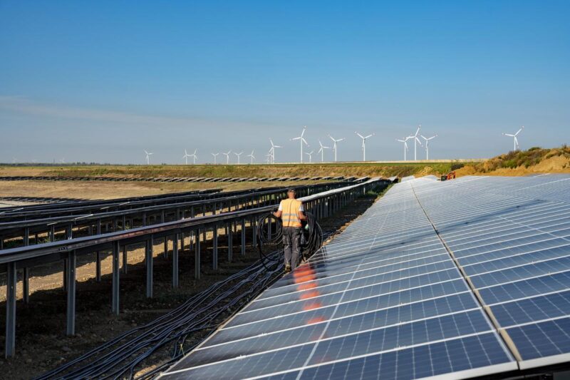 Ein Arbeiter geht durch eine Reihe von Solaranlagen in einer Ebene.