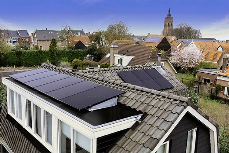 Haus mit Solarmodulen am Dach in einem Dorf mit Kirchturm.