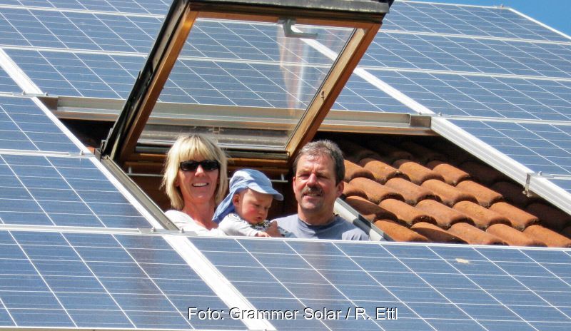 Eine Familie mit Baby blickt aus einem Dachfenster. Um sie herum ist das Dach mit Solarmodulen gedeckt.