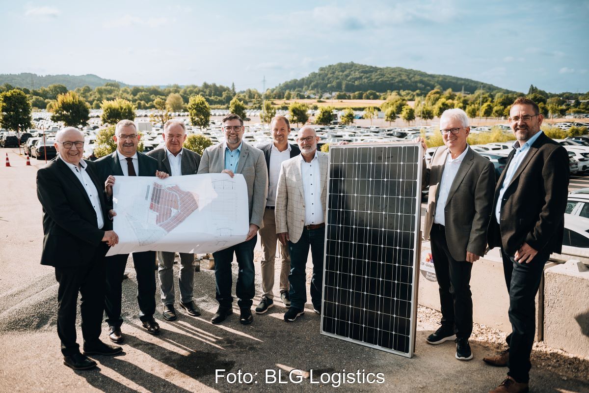 8 Männer mit Plan udn PV-Modul vor im Hintergrund stehenden Autos.