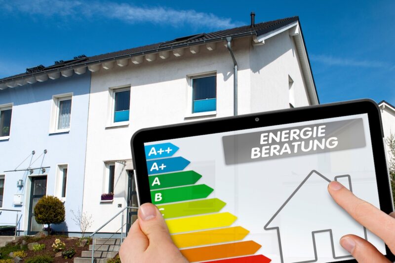 Reihenhaus im Hintergrund. Davor die Anzeige einer Gebäudeenergieverbrauchsskala als Symbol für die Energieberatung für Wohngebäude