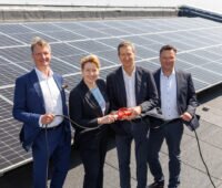 Die vier Verantwortlichen stehen auf dem Dach eines Gebäudes vor einer PV-Anlage
