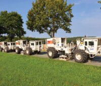 Mehrere Vibrotrucks auf einer Nebenstraße im Grünen
