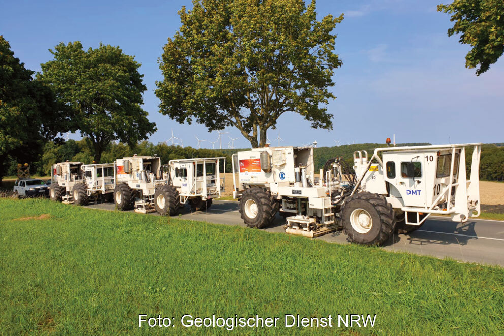 Mehrere Vibrotrucks auf einer Nebenstraße im Grünen