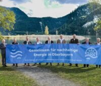 Männer mit blauem Banner vor Walchensee und Bergen, Wasserkraftwerk Walchensee