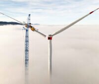 Über dem Nebel wird von einem Kran aus ein Rotor an einem Windrad installiert.