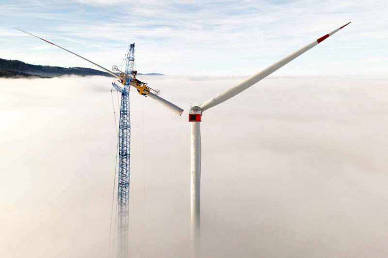 Über dem Nebel wird von einem Kran aus ein Rotor an einem Windrad installiert.