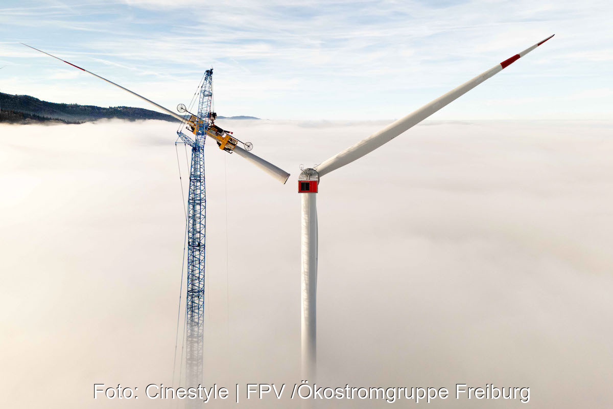 Über dem Nebel wird von einem Kran aus ein Rotor an einem Windrad installiert.