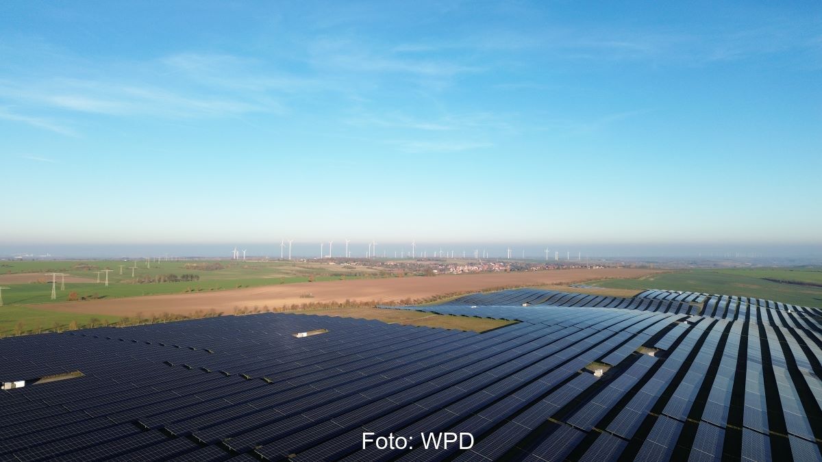 Ein Freiflächen-Solarpark vor einem Windpark im HIntergrund, die beide in das gleiche Umsapnnwerk einspeisen.