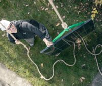 Ein Solarmodul wird per Flaschenzug transportiert, ein Mann mit Schutzhelm kontrolliert den Vorgang.