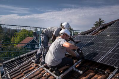 Zwei Handwerker installieren eine PV-Anlage auf einem Einfamilienhaus.